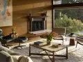 Salon w stylu mid century modern z kominkiem, wygodnymi fotelami i dużym oknem z widokiem na zieleń.