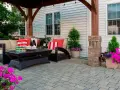 Wygodny taras z kostki z meblami wypoczynkowymi i kwitnącymi kwiatami. Idealne miejsce na relaks.