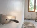 Nakładanie gładzi na ściany za pomocą kielni. W tle okno i wiadro z masą szpachlową.