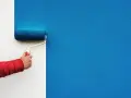 Ręka w czerwonej kurtce używa dobrego wałka do malowania ścian na intensywny niebieski kolor.