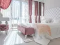 Elegancka sypialnia w stylu angielskim z pikowanym zagłówkiem, różowymi pufami i zasłonami.