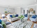 Jasny salon w stylu hampton z wygodnymi sofami, błękitnymi fotelami i dywanem z geometrycznym wzorem.