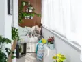 Przytulny balkon typu loggia z wygodną kanapą, ziołami na drewnianej ścianie i bukietem kwiatów. Idealne miejsce na relaks.