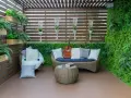 Zielony, bujny balkon w bloku z rattanowymi meblami, gitarą i książką. Idealne miejsce na relaks.