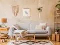 Przytulny salon w stylu boho: szara kanapa, makrama na ścianie, drewniane meble i rośliny tworzą relaksującą atmosferę.