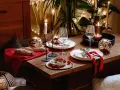 Romantyczna kolacja w domu: stół nakryty do świętowania, świece, kieliszki, pieczywo i pomidorki. Wystrój tworzy przytulną atmosferę.