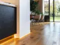 Nowoczesne wnętrze z drewnianą podłogą i subtelnym oświetleniem LED. Eleganckie rozwiązanie co zamiast listew przypodłogowych.