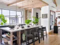 Nowoczesny salon w stylu modern farmhouse z wyspą kuchenną, drewnianymi belkami na suficie i dużą ilością zieleni.