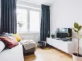 Przytulny salon w bloku z elementami feng shui: sofa z poduszkami, telewizor, roślina i zasłony tworzą harmonię.