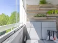 Przytulny mały balkon w bloku z szarą sofą, poduszką z liskiem i zielenią na drewnianej ściance.
