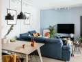 Salon w stylu minimalistycznym: niebieska kanapa, drewniany stół, czarne lampy i kot na kanapie.
