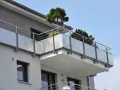 Nowoczesny balkon z ażurową balustradą i drzewkami iglastymi. Jaki spadek na balkonie, by woda deszczowa spływała?
