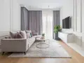 Elegancki salon w stylu modern classic. Jasna kanapa, okrągły stolik kawowy, dywan i zasłony tworzą przytulną atmosferę.
