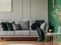 Szaro-zielony salon z wygodną sofą, ozdobioną poduszkami i kocami. Obok stoi stolik z książkami i wazonem.