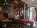 Przytulna sypialnia w stylu retro z ceglaną ścianą, regałami pełnymi książek, wygodnym fotelem i łóżkiem z czerwoną narzutą.