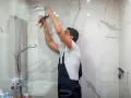 Instalator w ogrodniczkach dokręca słuchawkę prysznicową. To przykład, co to jest biały montaż w łazience.