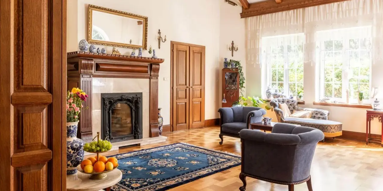 Elegancki salon w stylu kolonialnym z kominkiem, drewnianymi belkami stropowymi i stylowymi meblami.