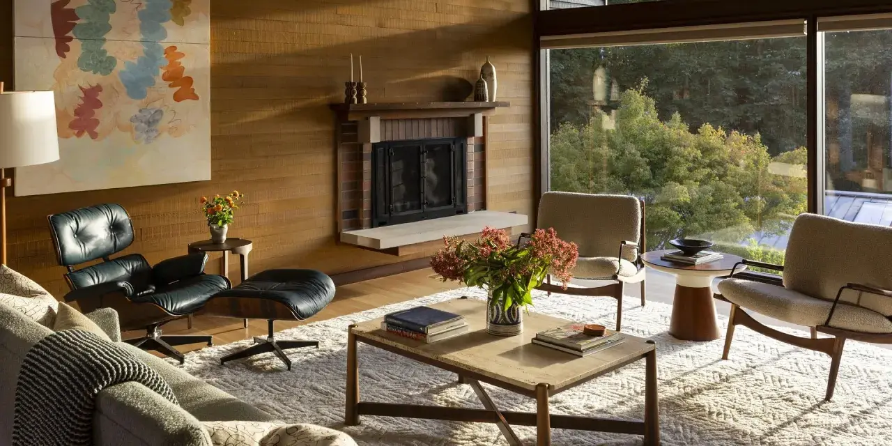 Salon w stylu mid century modern z kominkiem, wygodnymi fotelami i dużym oknem z widokiem na zieleń.