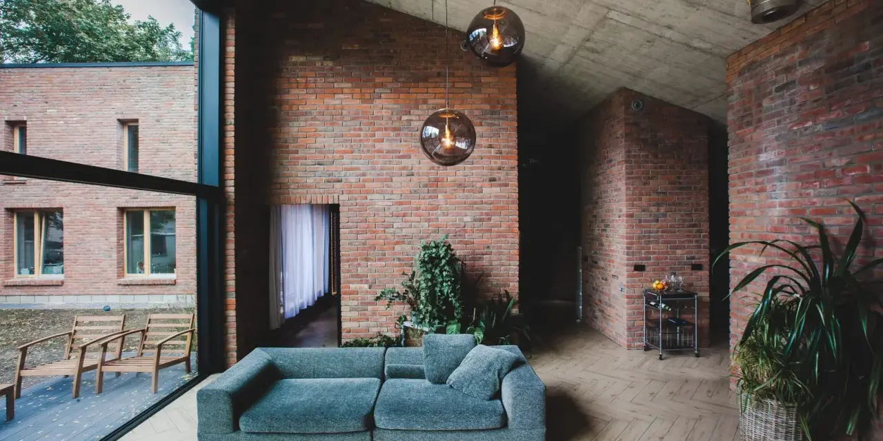 Nowoczesny salon z cegłą w roli głównej. Szara kanapa, betonowy sufit i duże okna tworzą industrialny klimat.