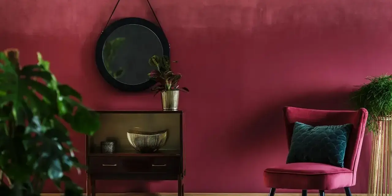 Eleganckie wnętrze w kolorze marsala, z aksamitnym fotelem, lustrem i roślinami.