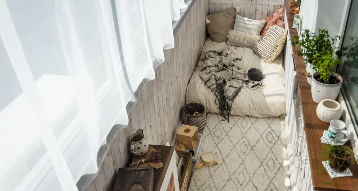 Przytulny balkon w stylu boho: łóżko z kocem, poduszki, dywan, rośliny i drewniane dekoracje. Idealne inspiracje na relaks.