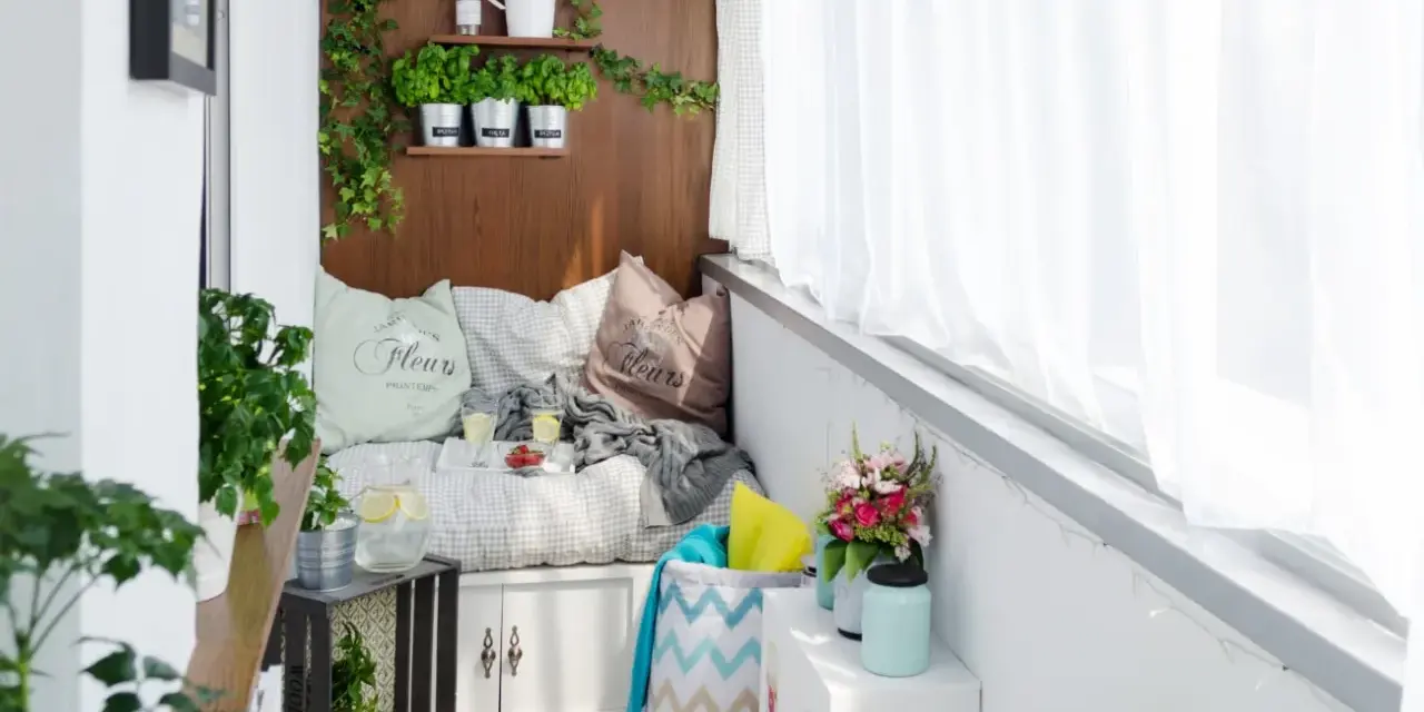 Przytulny balkon typu loggia z wygodną kanapą, ziołami na drewnianej ścianie i bukietem kwiatów. Idealne miejsce na relaks.