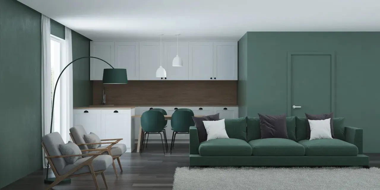 Nowoczesny salon z kuchnią, gdzie dominują zielony kolor ścian i mebli. Wygodna sofa, fotele i stół z krzesłami tworzą przytulną przestrzeń.