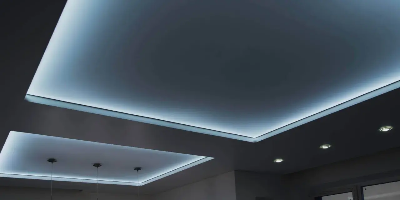 Nowoczesny sufit napinany w salonie z subtelnym, niebieskim podświetleniem LED tworzy relaksującą atmosferę.