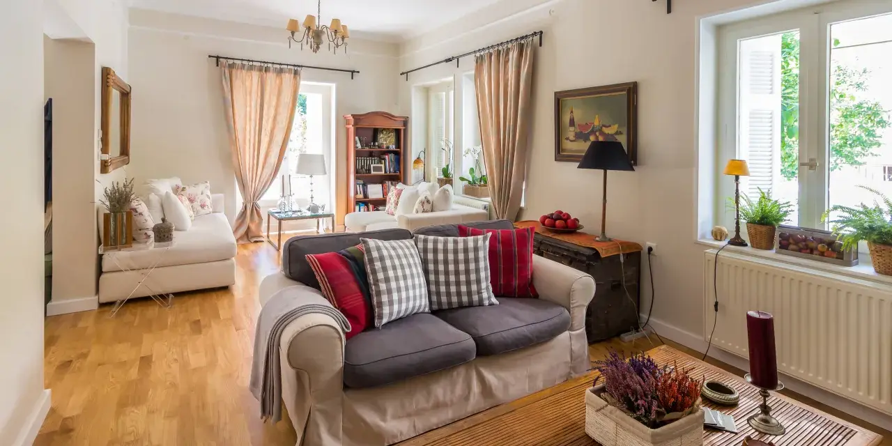 Przytulny salon w stylu angielskim nowoczesnym. Jasne ściany, drewniana podłoga, wygodne sofy z poduszkami w kratę i paski.
