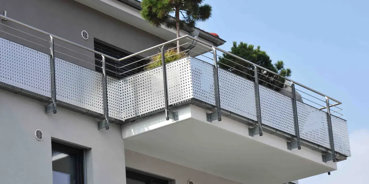Nowoczesny balkon z ażurową balustradą i drzewkami iglastymi. Jaki spadek na balkonie, by woda deszczowa spływała?