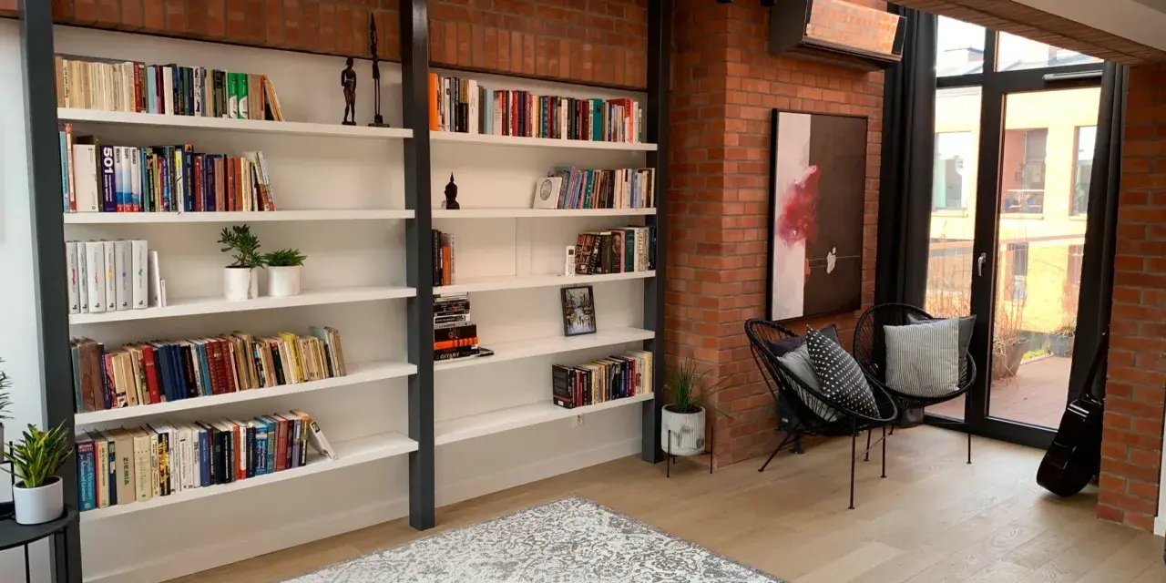 Nowoczesna biblioteczka w stylu bauhaus z ceglaną ścianą, czarnymi krzesłami i dywanem.