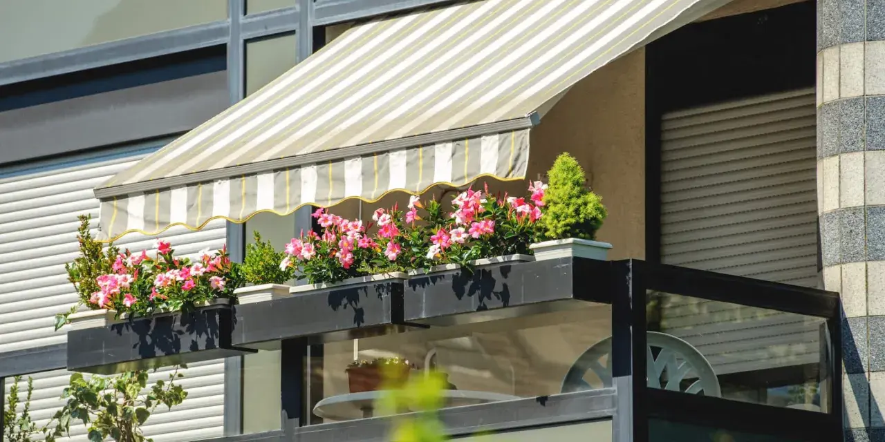 Jak zrobić daszek na balkon? Płócienny markiza chroni przed słońcem, a skrzynki z kwiatami dodają uroku.