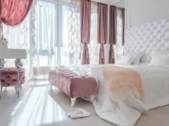 Elegancka sypialnia w stylu angielskim z pikowanym zagłówkiem, różowymi pufami i zasłonami.
