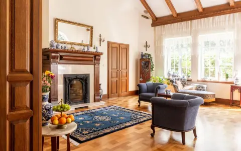 Elegancki salon w stylu kolonialnym z kominkiem, drewnianymi belkami stropowymi i stylowymi meblami.