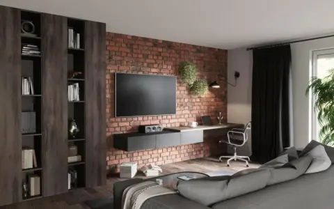 Nowoczesny salon loft inspiracje: ceglana ściana, wisząca szafka RTV, biurko z laptopem, regały i szara kanapa.