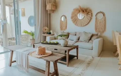 Przytulny salon w stylu bohema. Jasna sofa, drewniane meble, plecione dekoracje i słomkowy kapelusz tworzą relaksującą atmosferę.