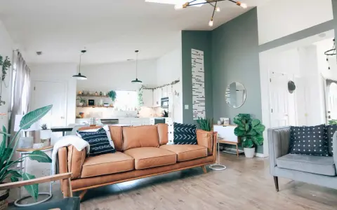 Nowoczesny salon z brązową kanapą i szarym fotelem. Ściana w kolorze zielonym dodaje charakteru, a rośliny wprowadzają życie. Idealny kolor do salonu.