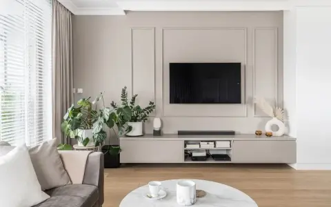 Elegancki telewizor w zabudowie meblowej, otoczony zielenią i nowoczesnymi dodatkami, tworzy przytulną przestrzeń do relaksu.