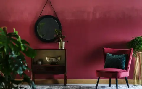 Eleganckie wnętrze w kolorze marsala, z aksamitnym fotelem, lustrem i roślinami.