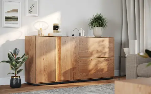 Drewniana komoda w salonie, ozdobiona lampą, świecą i roślinami. Idealne co na komodę w salonie, by stworzyć przytulną atmosferę.