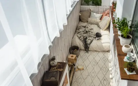 Przytulny balkon w stylu boho: łóżko z kocem, poduszki, dywan, rośliny i drewniane dekoracje. Idealne inspiracje na relaks.