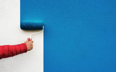 Ręka w czerwonej kurtce używa dobrego wałka do malowania ścian na intensywny niebieski kolor.