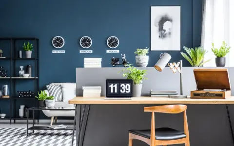 Biuro z zegarami pokazującymi czas w Nowym Jorku, Londynie i Tokio na ścianie w kolorze navy. Na biurku laptop, lampka i gramofon.