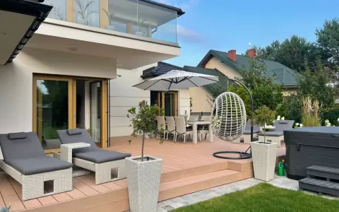 Nowoczesny taras aranżacje: leżaki, stół z krzesłami, huśtawka i jacuzzi tworzą strefę relaksu.