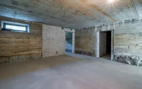 Surowa piwnica ziemna z betonowymi ścianami, białymi ceglanymi wstawkami i oknem. Widać przygotowania do wentylacji piwnicy ziemnej.