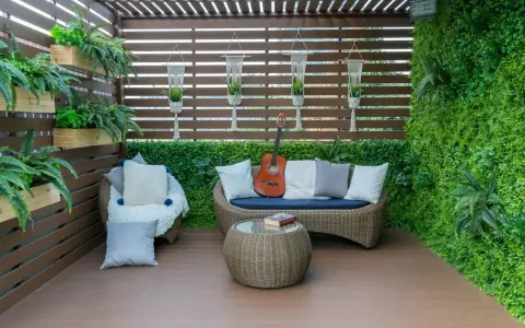 Zielony, bujny balkon w bloku z rattanowymi meblami, gitarą i książką. Idealne miejsce na relaks.