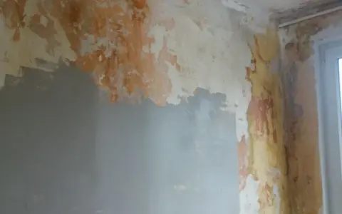 Ściana w trakcie remontu, z fragmentami starej farby i nową warstwą gładzi. Pokazuje, jak położyć gładź na ścianę, przygotowując ją do malowania.