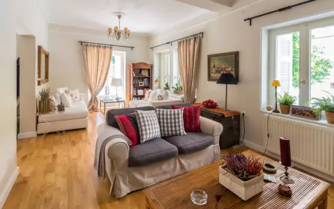 Przytulny salon w stylu angielskim nowoczesnym. Jasne ściany, drewniana podłoga, wygodne sofy z poduszkami w kratę i paski.