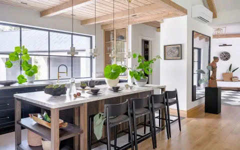 Nowoczesny salon w stylu modern farmhouse z wyspą kuchenną, drewnianymi belkami na suficie i dużą ilością zieleni.