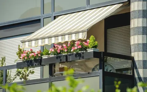 Zadaszenie balkonu z markizą i kwitnącymi kwiatami to świetny sposób, jak osłonić balkon przed słońcem i deszczem.